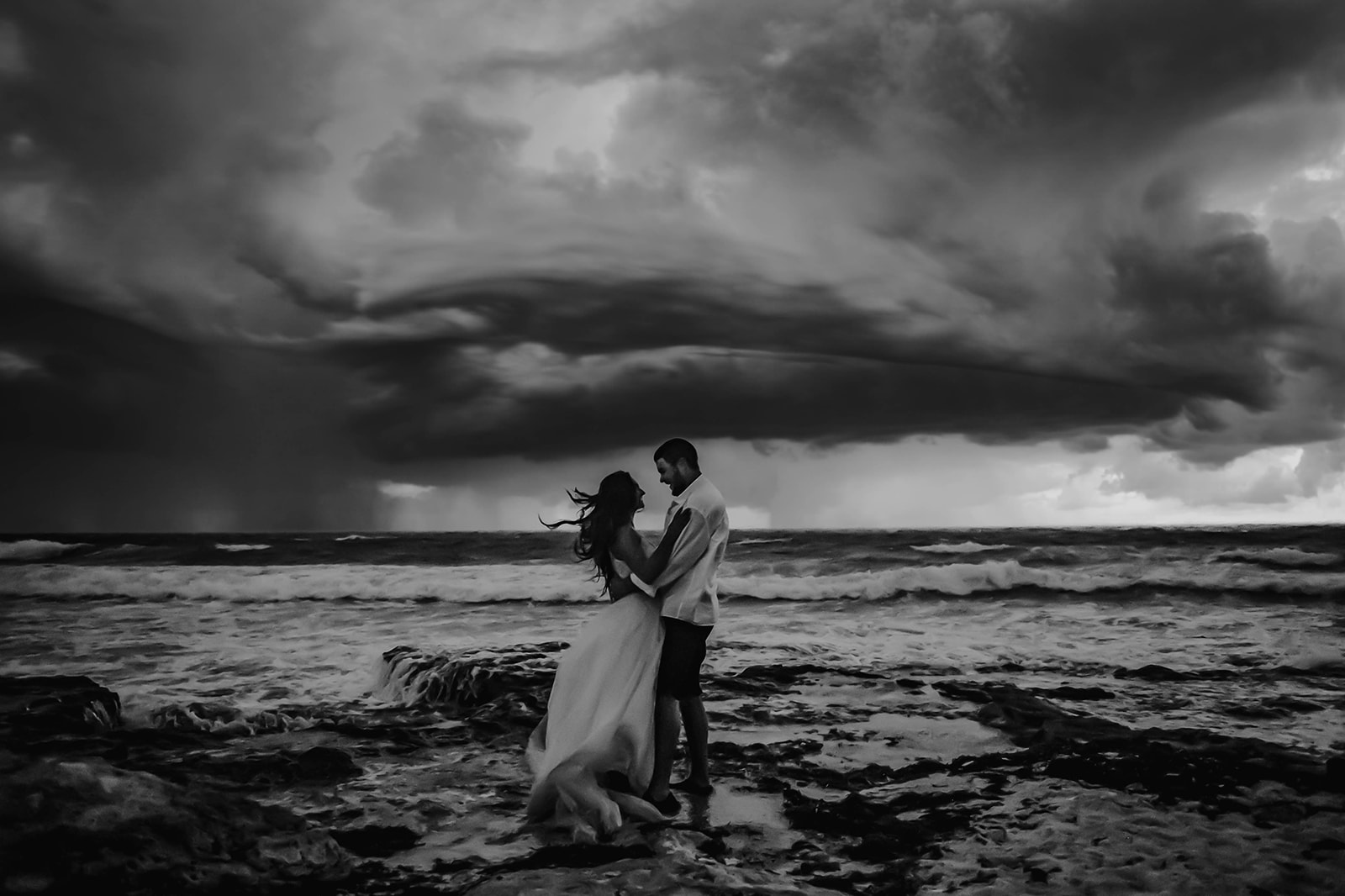 Bride and groom embracing on the coast of mexico during a hurricane