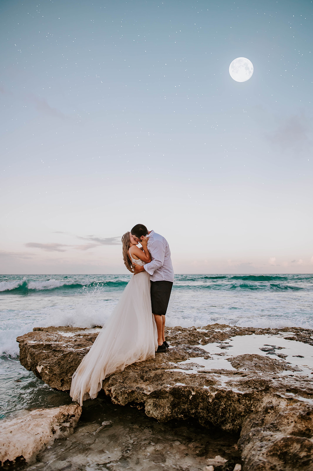 Bride and groom kissing under the full moon on the shore of the caribbean sea at twilight
