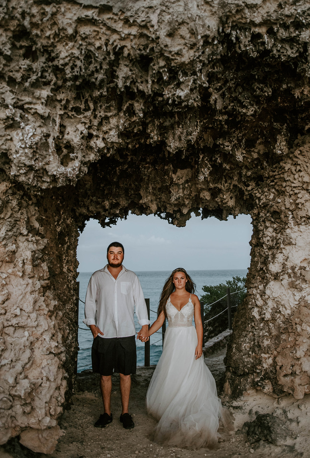 Bride and groom standing under a rock formation on South Point of Isla Mujeres