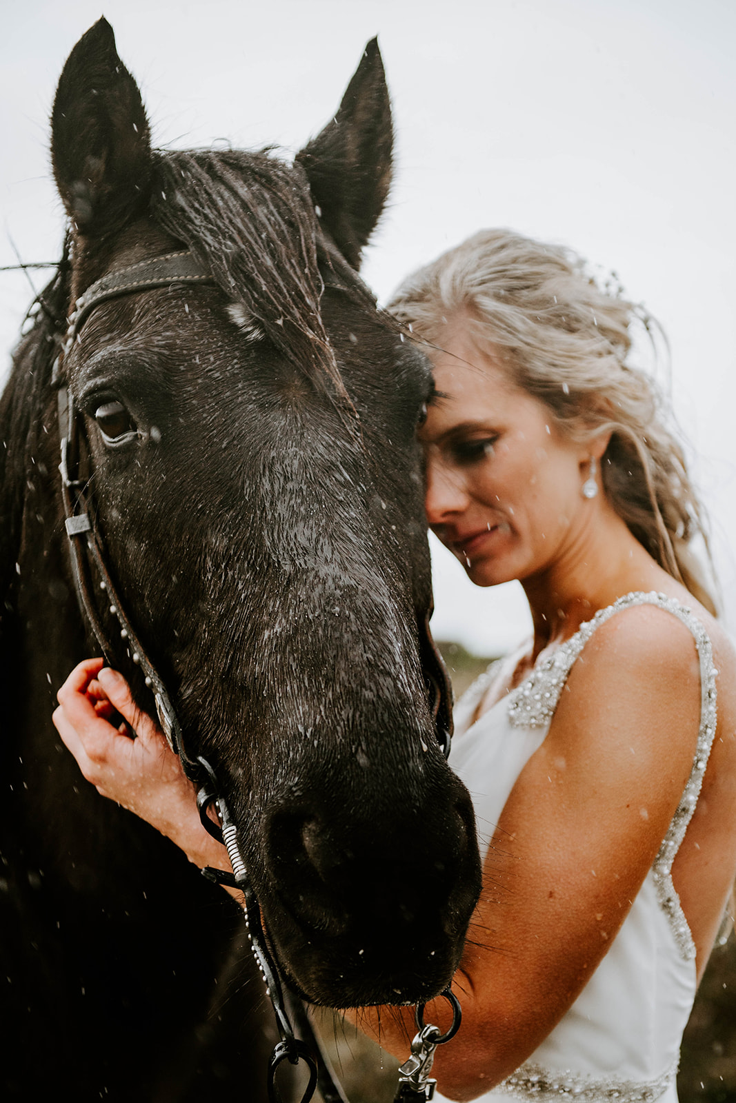 A blonde bride hugging her black horse while it rains on the Oregon Coast.