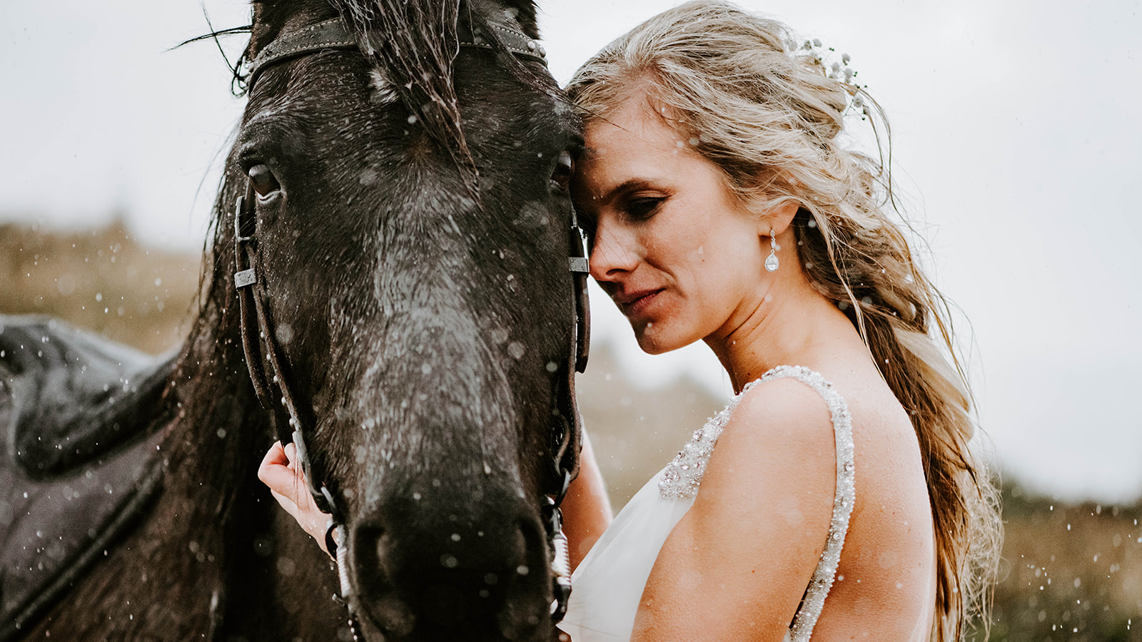 A blonde bride hugging her black horse while it rains on the Oregon Coast.