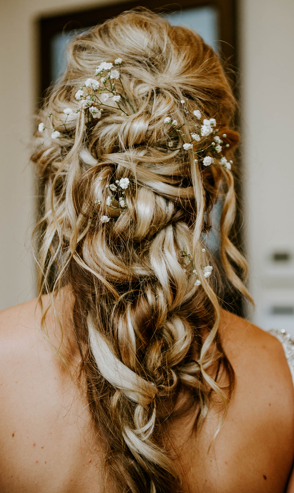 Blonde messy updo as a partial braid with baby's breath flowers in it.