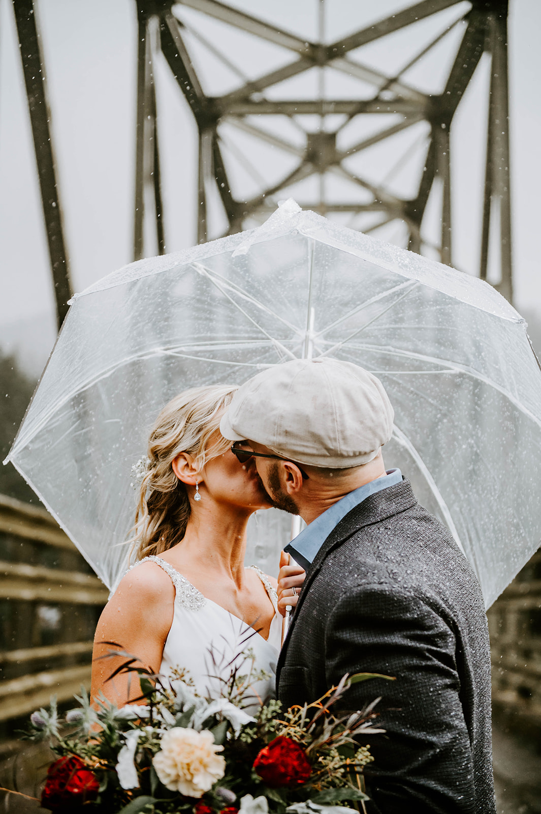 A bride and groom kissing on Myrtle Tree Bridge under a clear umbrella.