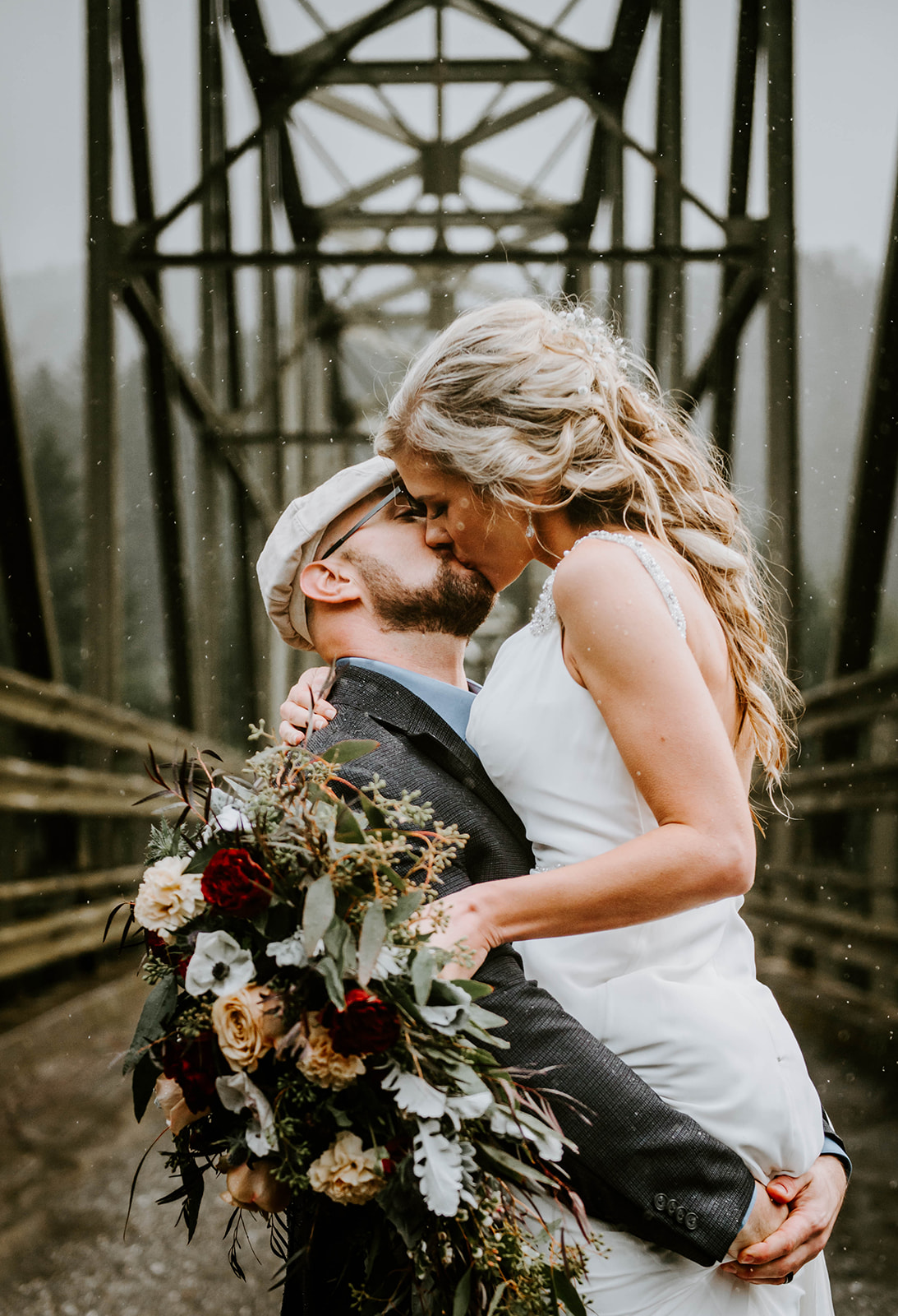 A bride and groom kissing in the rain on Myrtle Tree Bridge on the Rogue River in Gold Beach, Oregon.