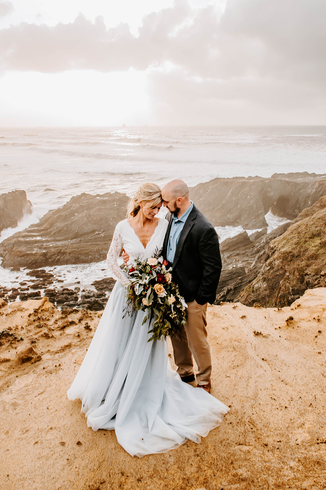 A bride and groom standing forehead to forehead on the cliffs at Otter Point on the Oregon Coast.