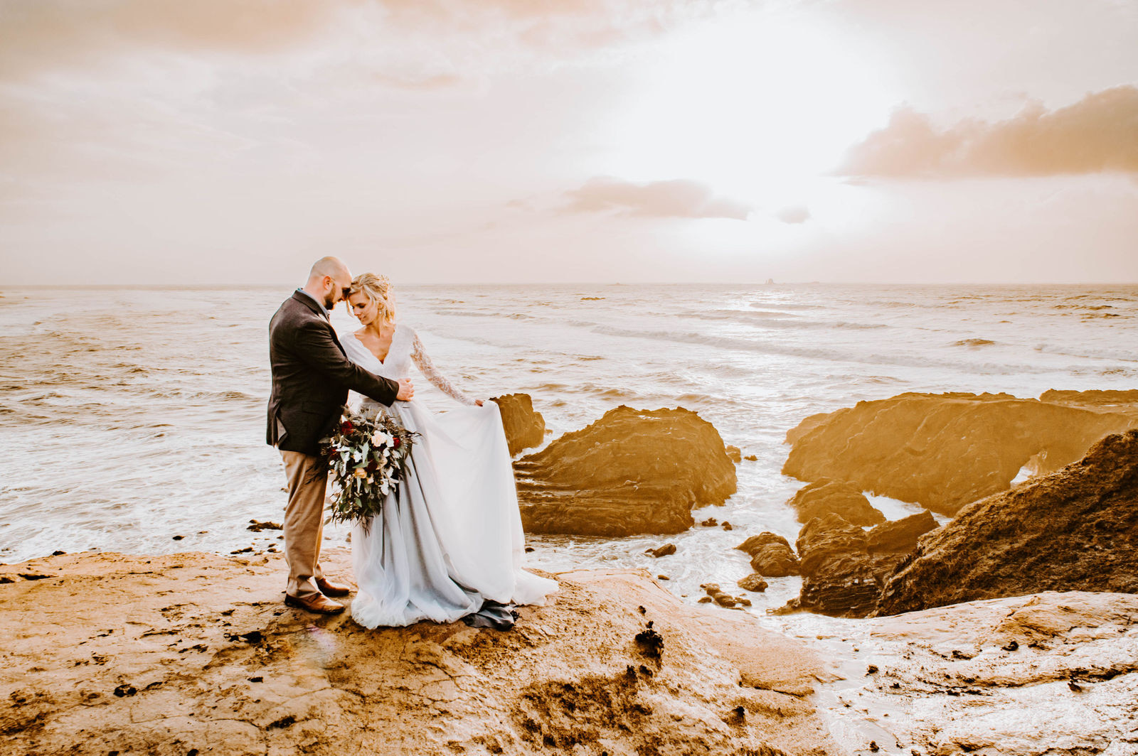 A bride and groom standing forehead to forehead overlooking the ocean during sunset at Otter Point in Gold Beach.