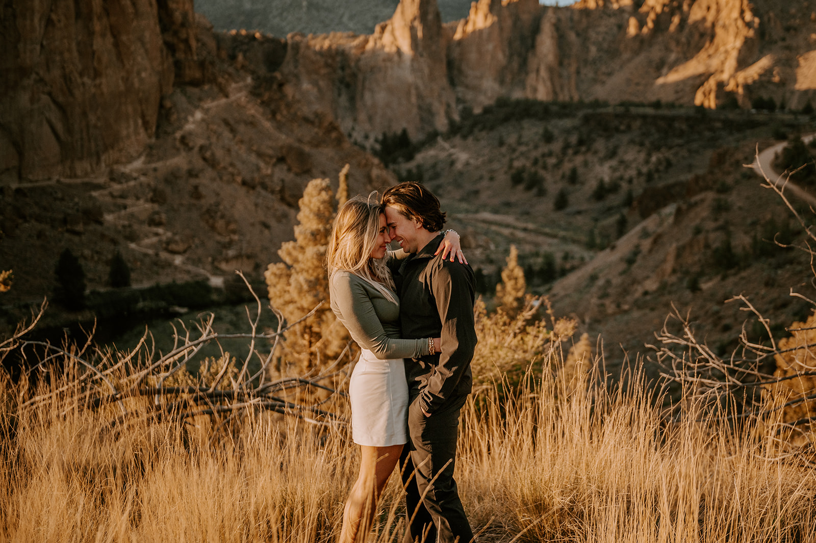 A couple smiling at each other standing in the tall grass overlooking the valley at smith rock