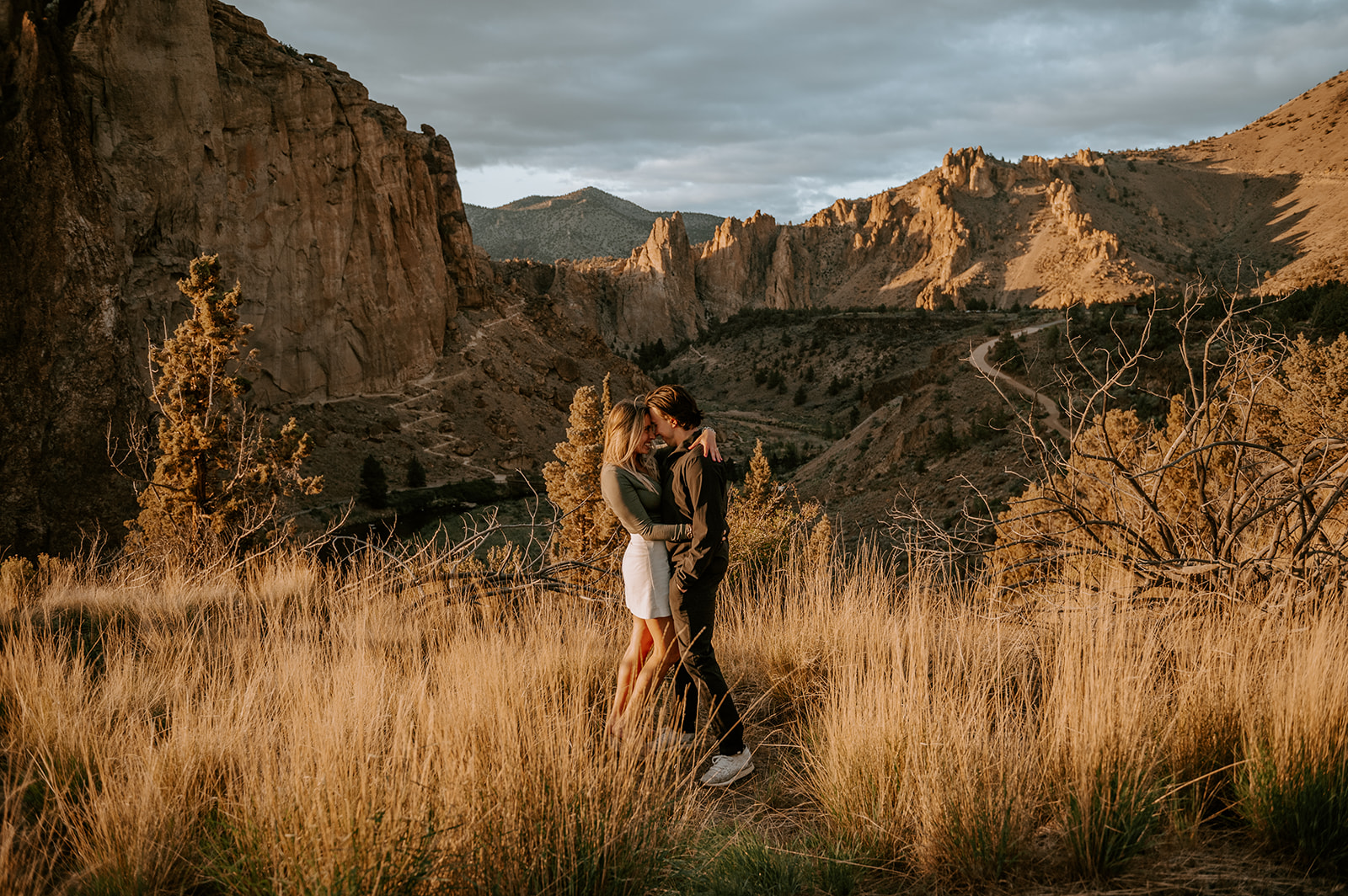 A couple smiling at each other standing in the tall grass overlooking the valley at smith rock