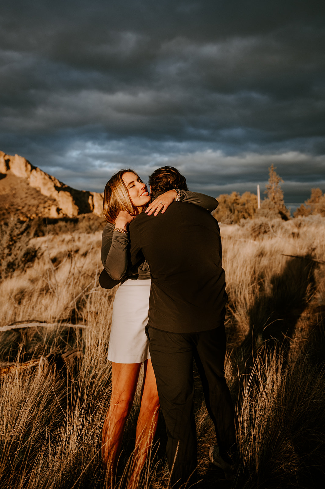 Newly engaged couple embraces with storm clouds overhead at smith rock