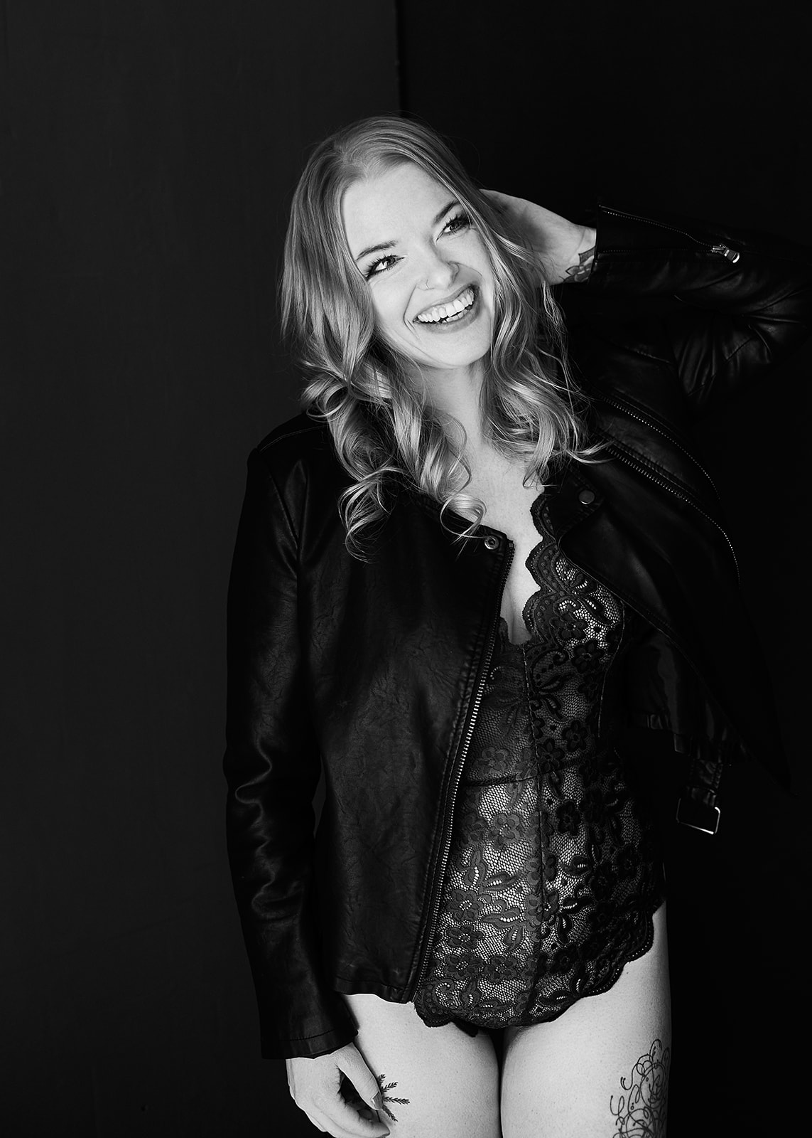 Boudoir photograph of a woman in a black teddy with black leather jacket, smiling at the camera 