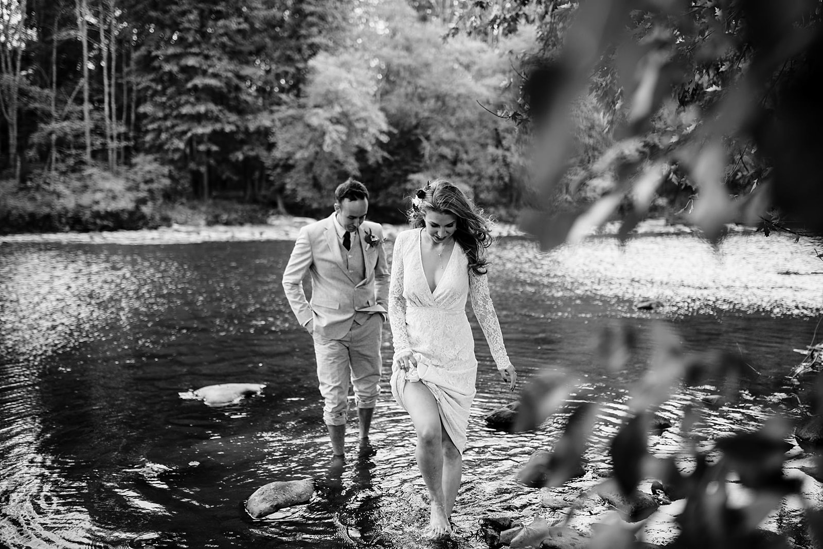 Black and white portrait of couple walking out of the river over rocks towards their wedding ceremony.