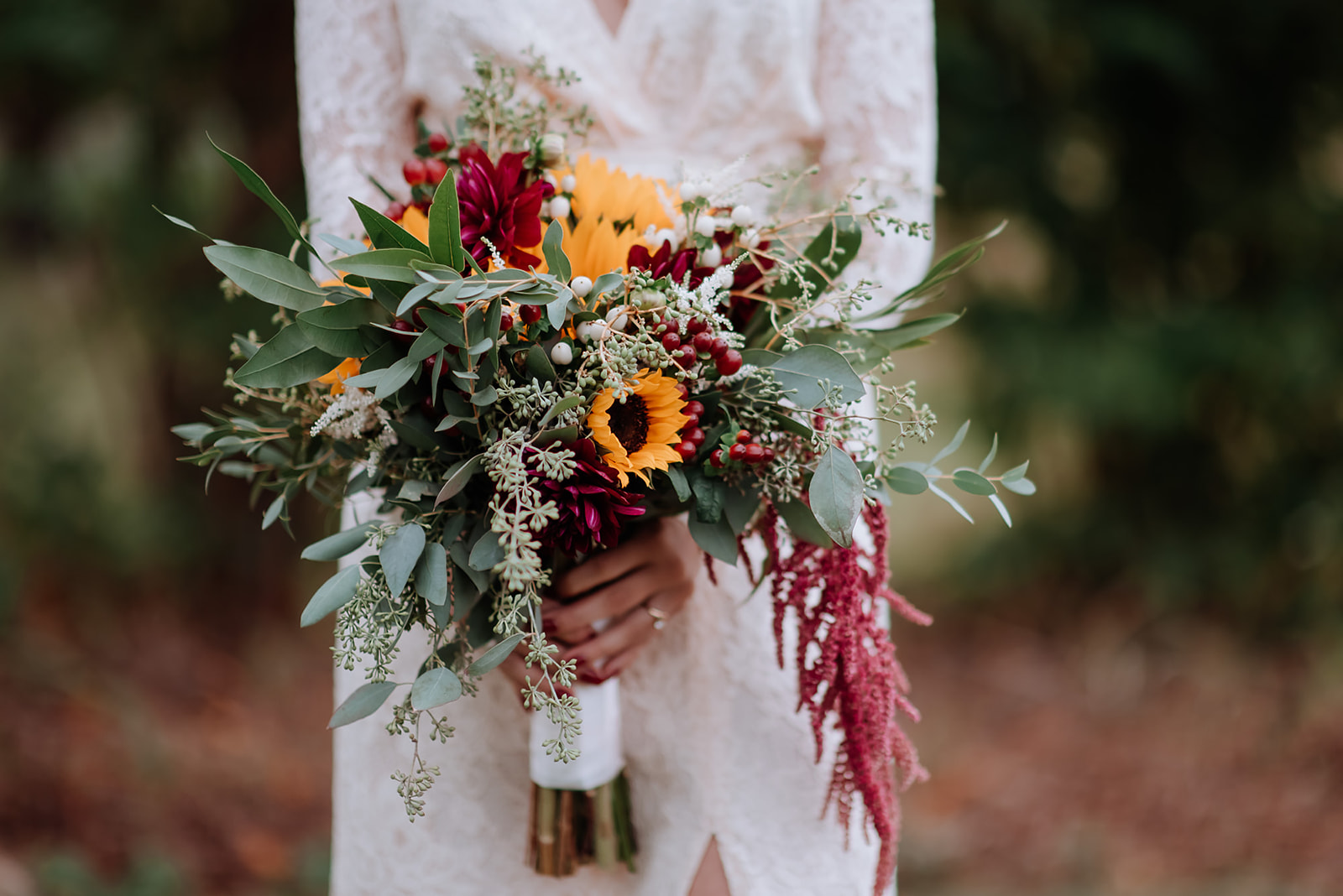 Bride holds her wildflower bouquet filled with sunflowers and amaranth streaming down.