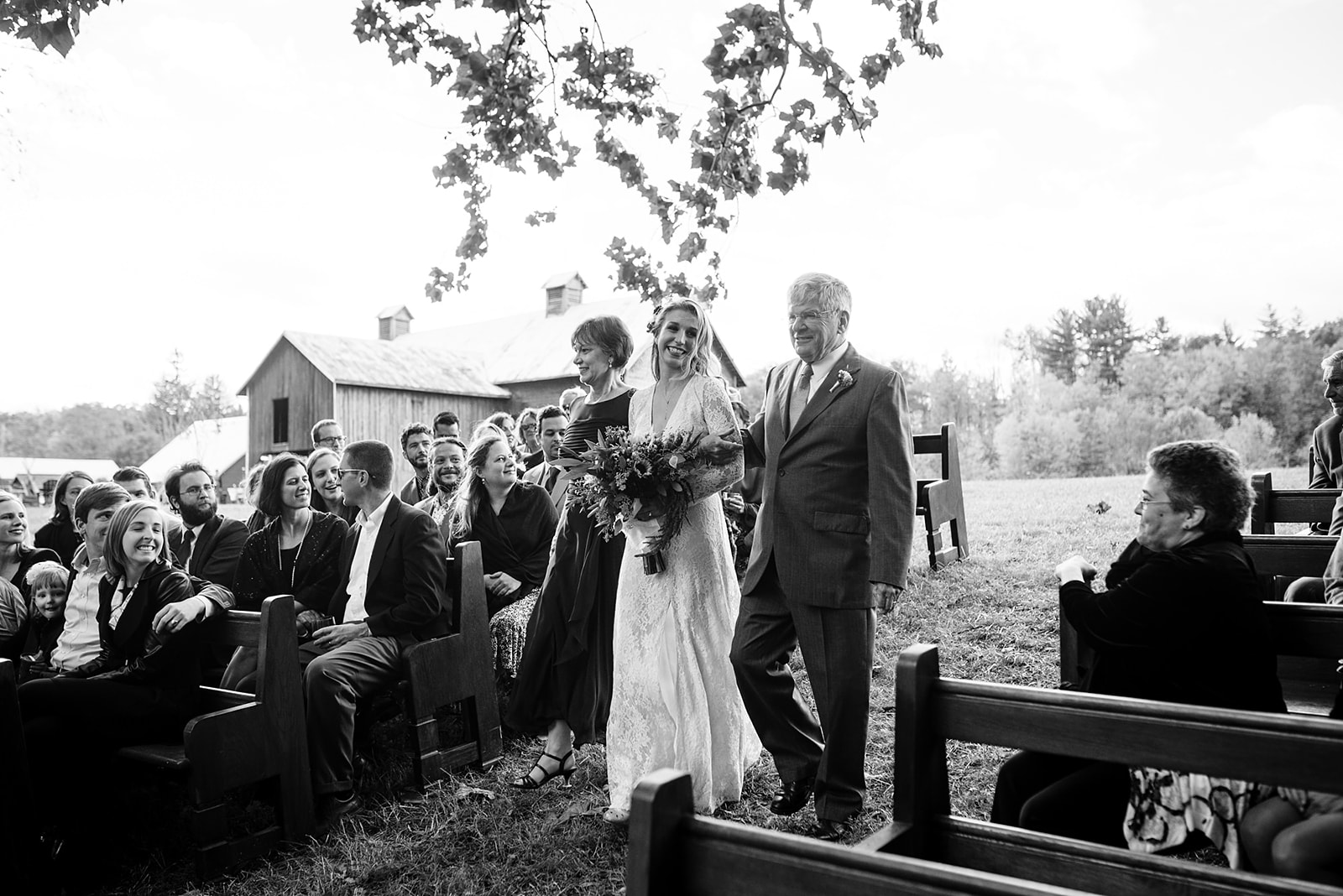 Bride walks down the aisle with her Parents towards her river front ceremony at Crested Hen Farms.