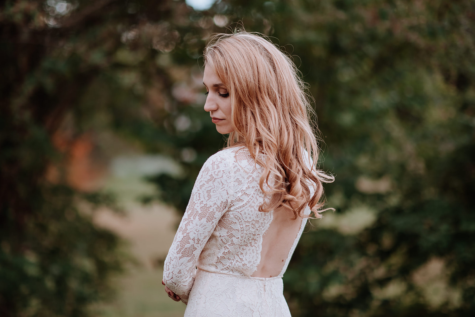 Bride's strawberry blonde hair cascades down her open back with her arms and shoulders framed in a vintage lace dress.