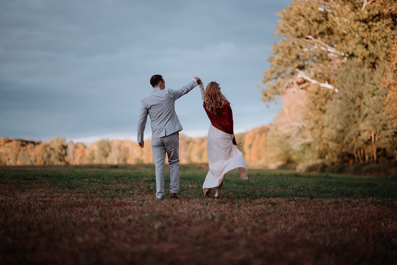 Couple twirls and dances in a huge farm field during golden hour on their wedding day.