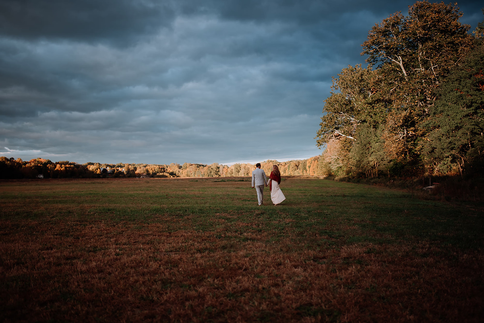 Couple wanders into field during golden hour on their wedding day.
