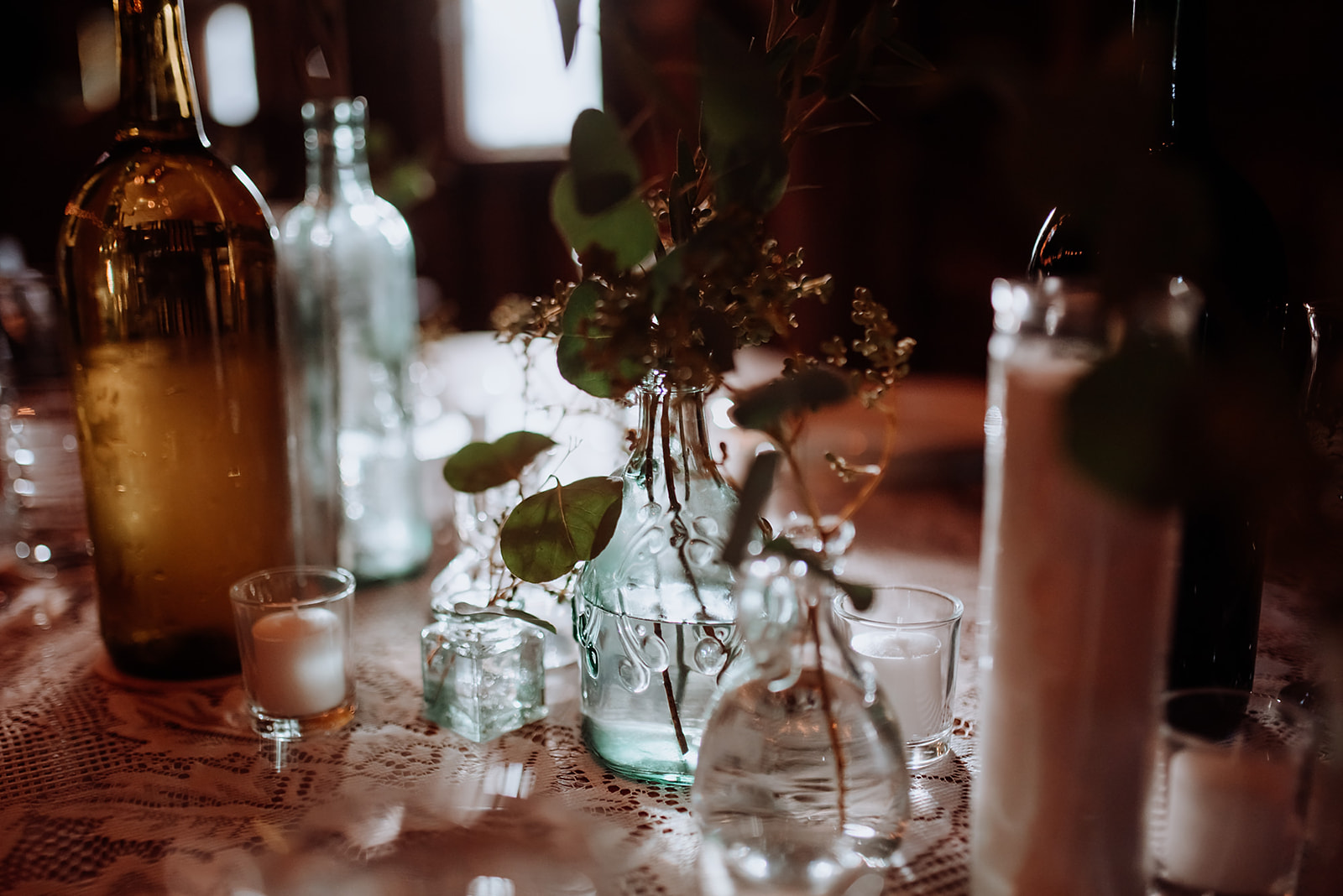 Glass bottles with fresh eucalyptus springs scattered along farmhouse tables for wedding reception.