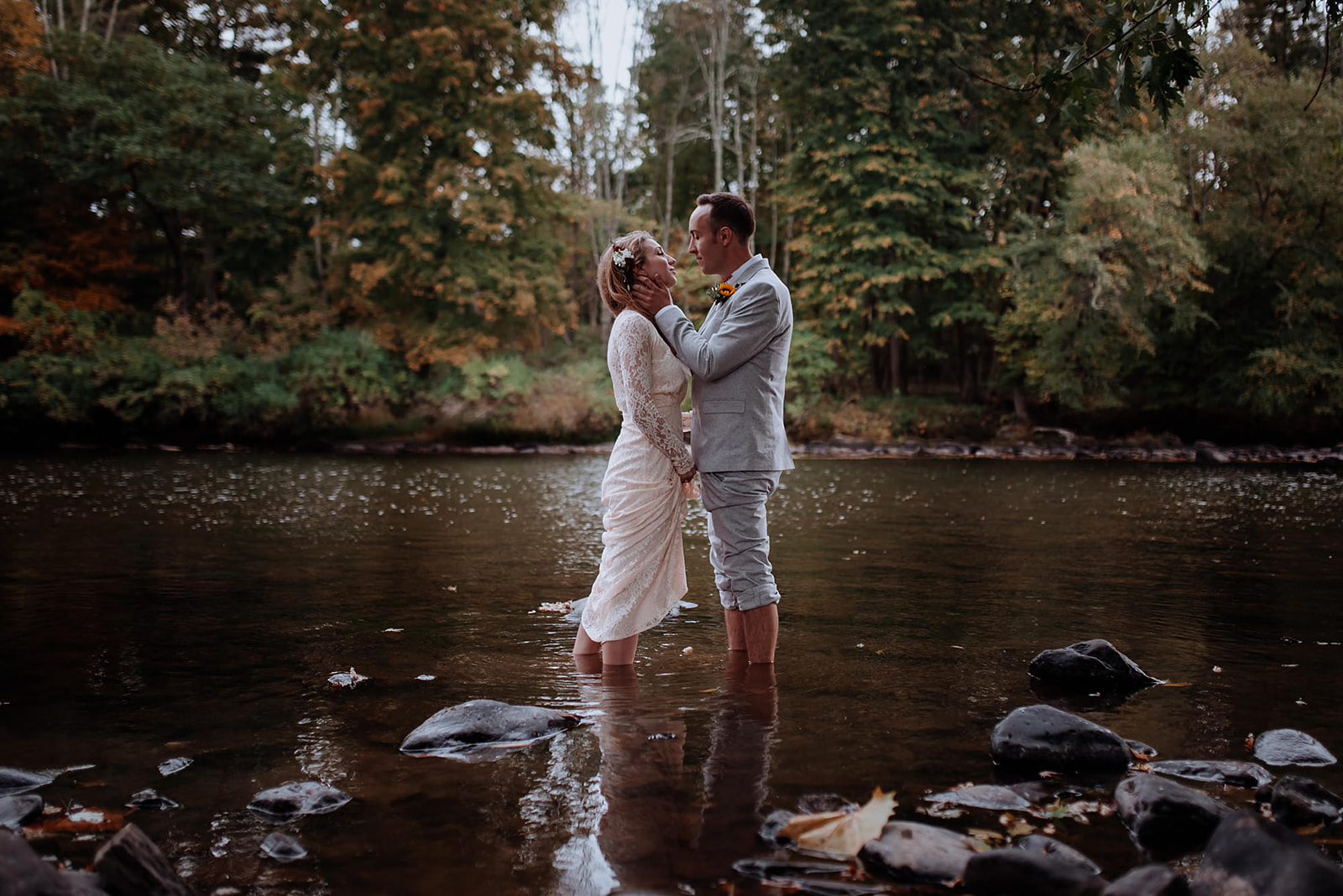 Young hipster couple stands in shallow river and share an intimate kiss before their Crested Hen Farms wedding.