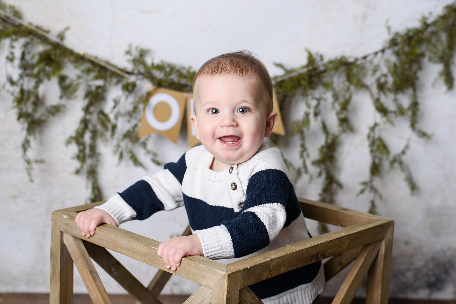 a baby boy smiles while standing during this one year photoshoot