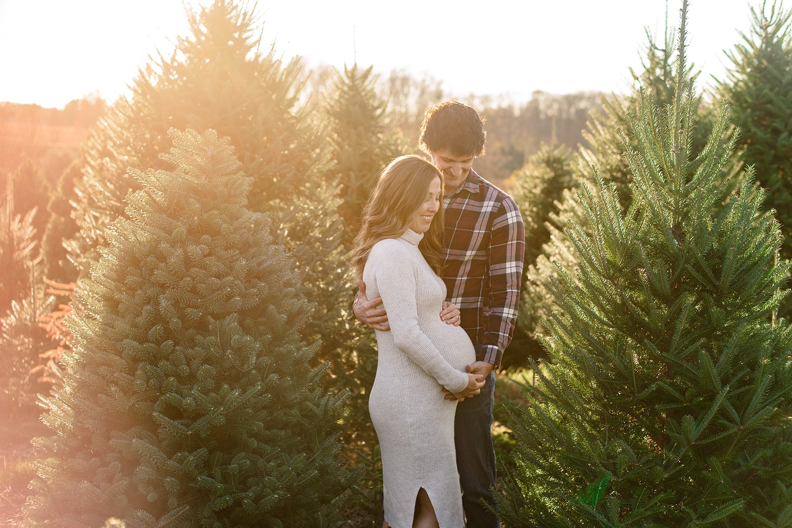 Soon-to-be parents snuggle in the Christmas trees during their maternity photoshoot with Rachel Mummert Photography