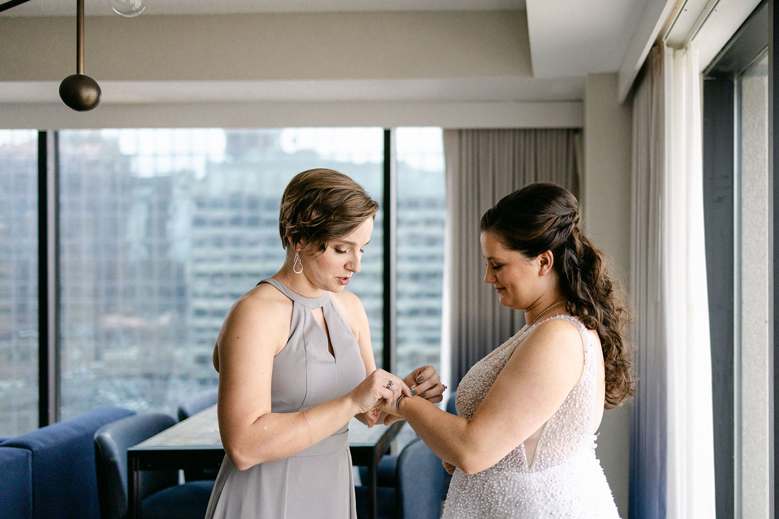 bridesmaid putting on bride's jewelry by Michele Maloney Photography