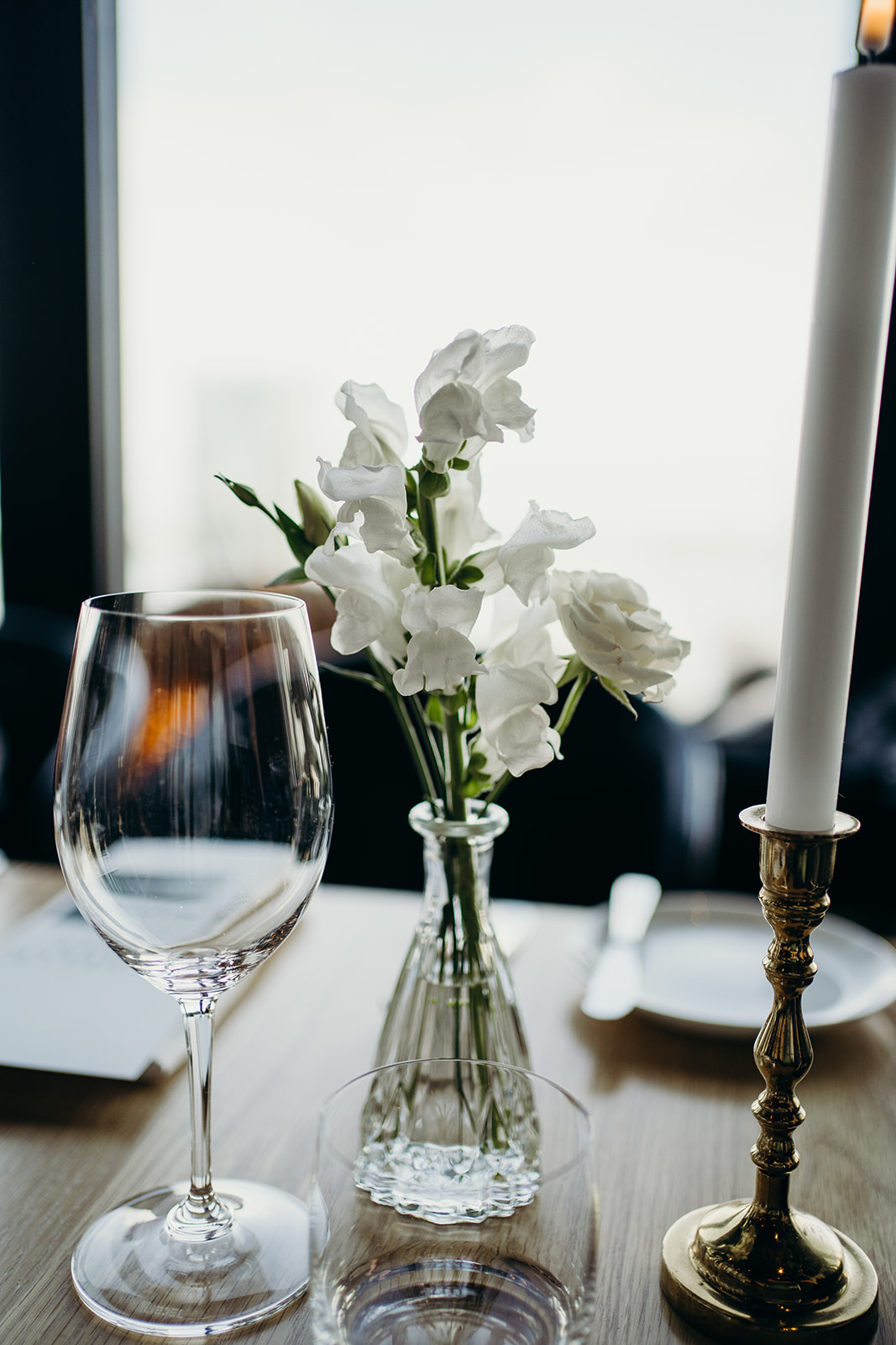 A candle, flowers and an empty wine glass on a table.