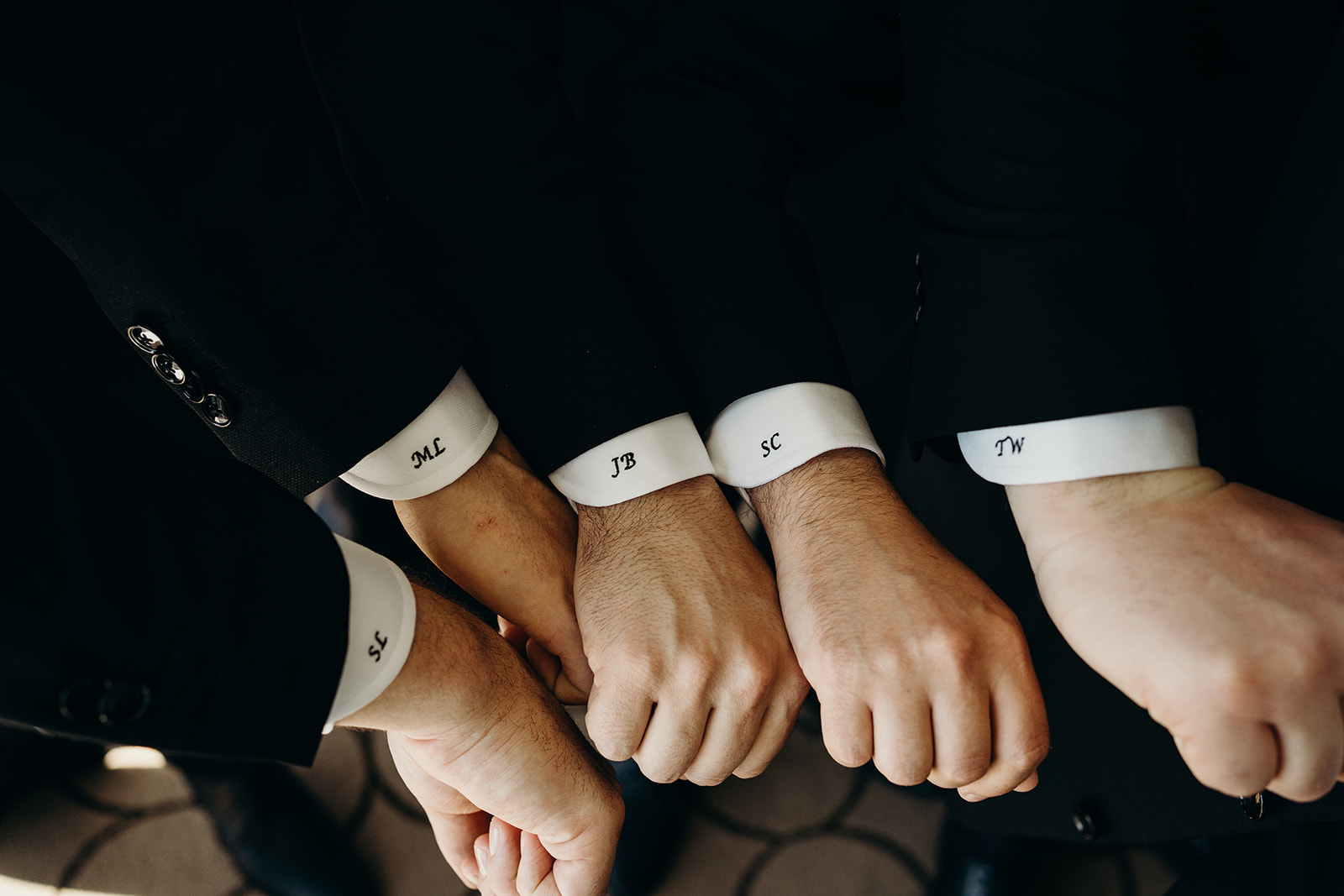 Close-up of 5 hands with black initials on white sleeve (Left to Right: S.L., M.L., J.B., S.C., and T.W.)
