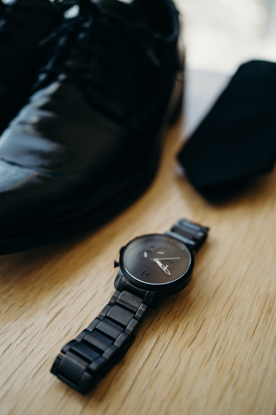 Close-up shot of shoes, watch and tie on a beige square table.