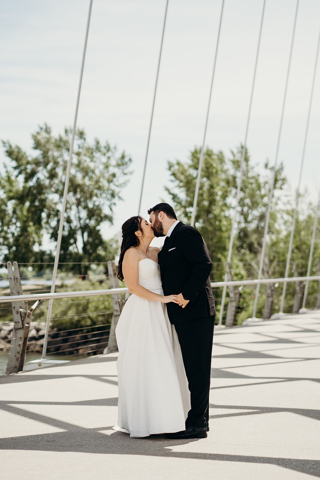 Husband and wife kissing on a bridge with trees in the background.