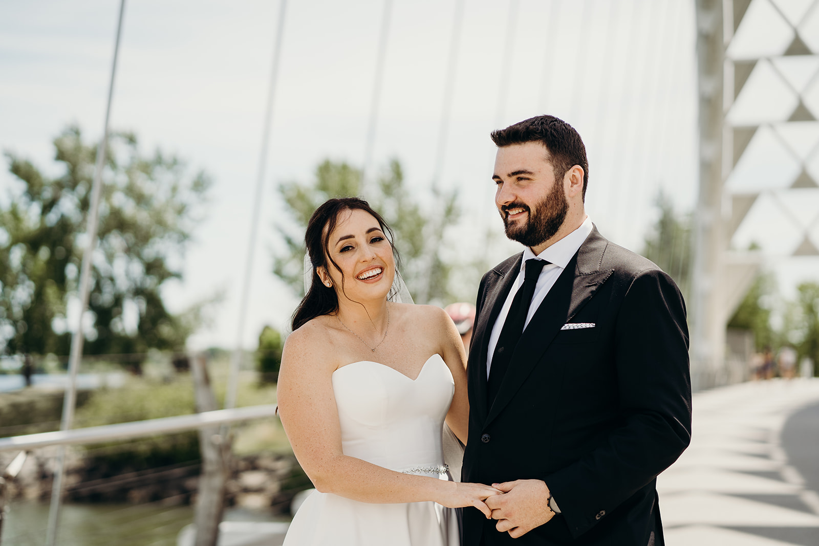 Husband and wife smiling and holding hands on the bridge outside in Toronto, Ontario.