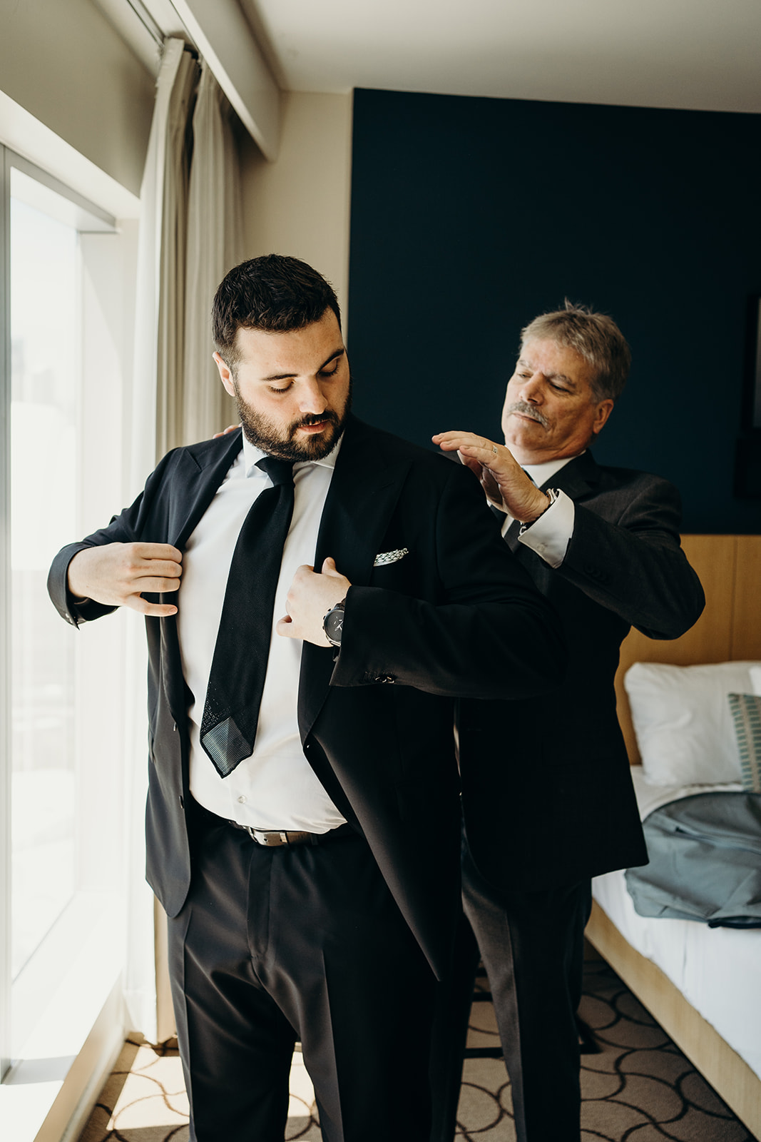 A man helping another put on his tux for the wedding.