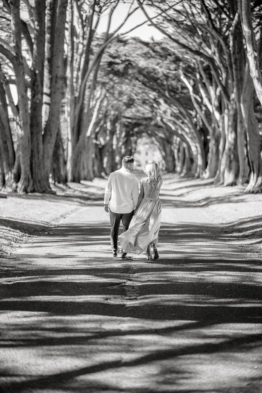 Black and white photo of Engagement couple walking away at Cypress tree tunnel at Point Reyes CAduring their photoshoot 