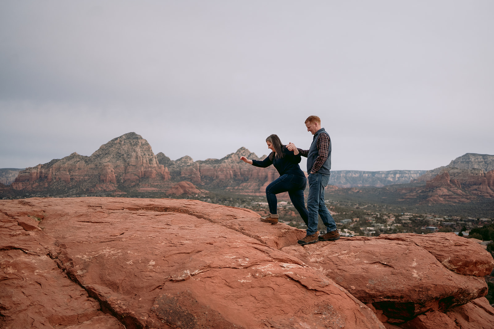 husband helping wife over some red rocks