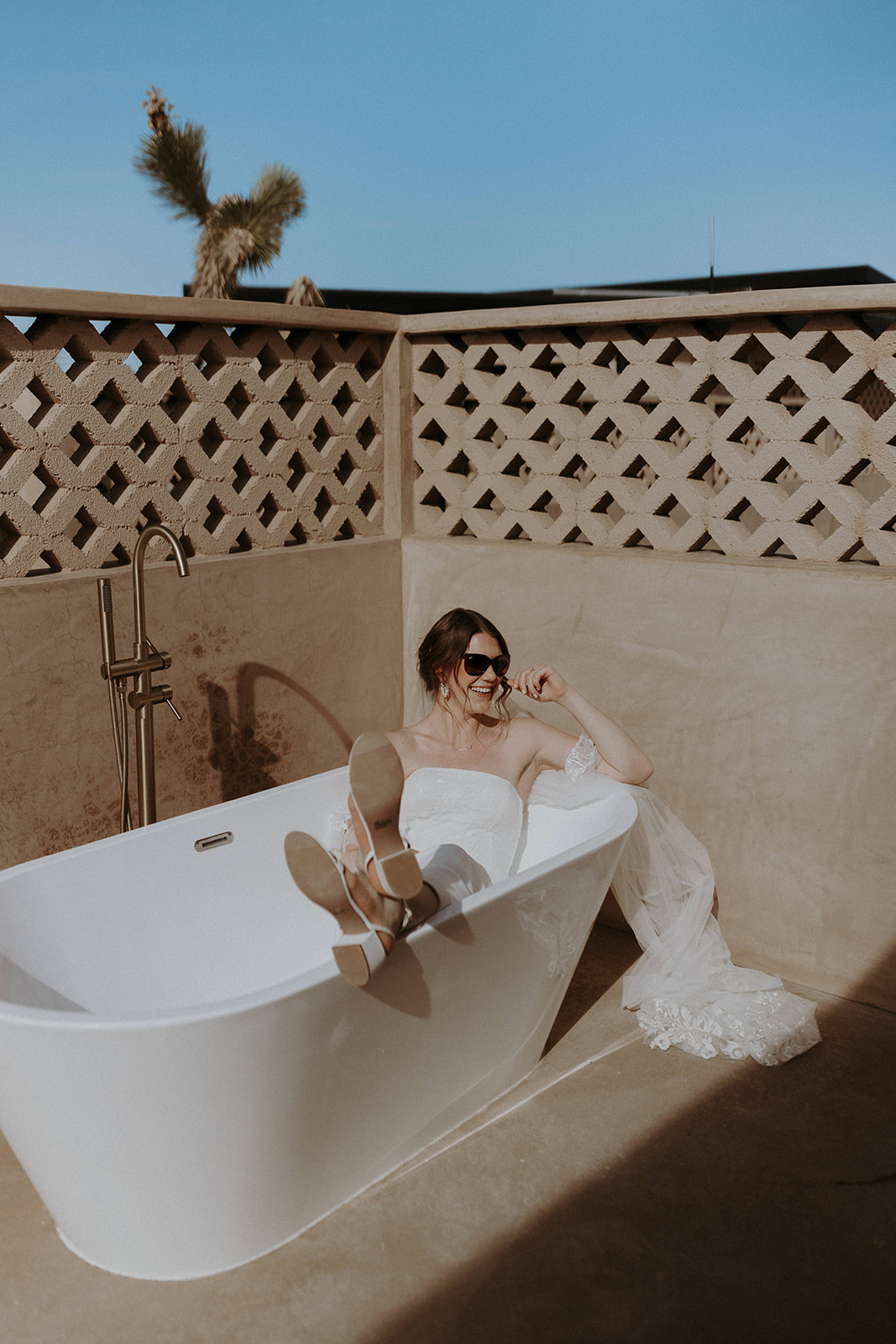 A bride wearing sunglasses in an outdoor bathtub at a luxury boho airbnb in Joshua Tree.