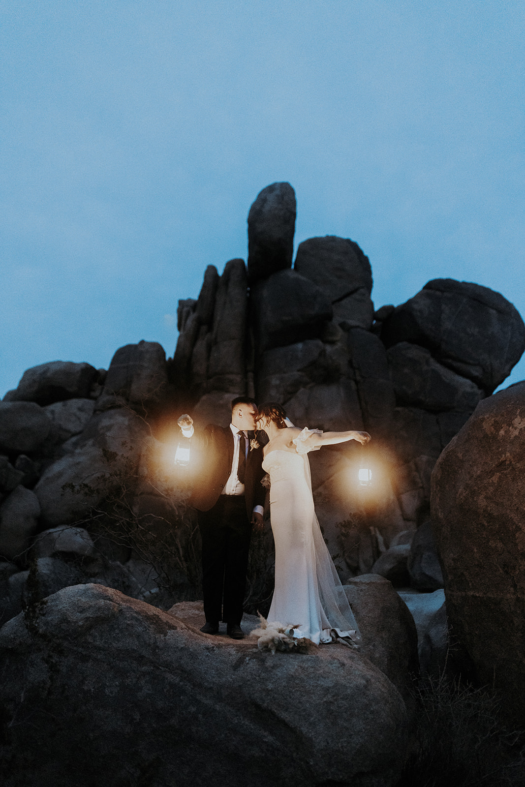 A wedding couple in Joshua Tree National Park at night holding lanterns and kissing.