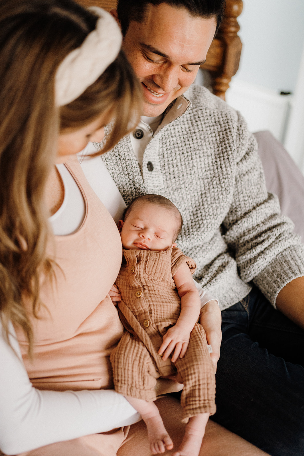 Both parents looking at newborn smiling while mother holds newborn upright between them