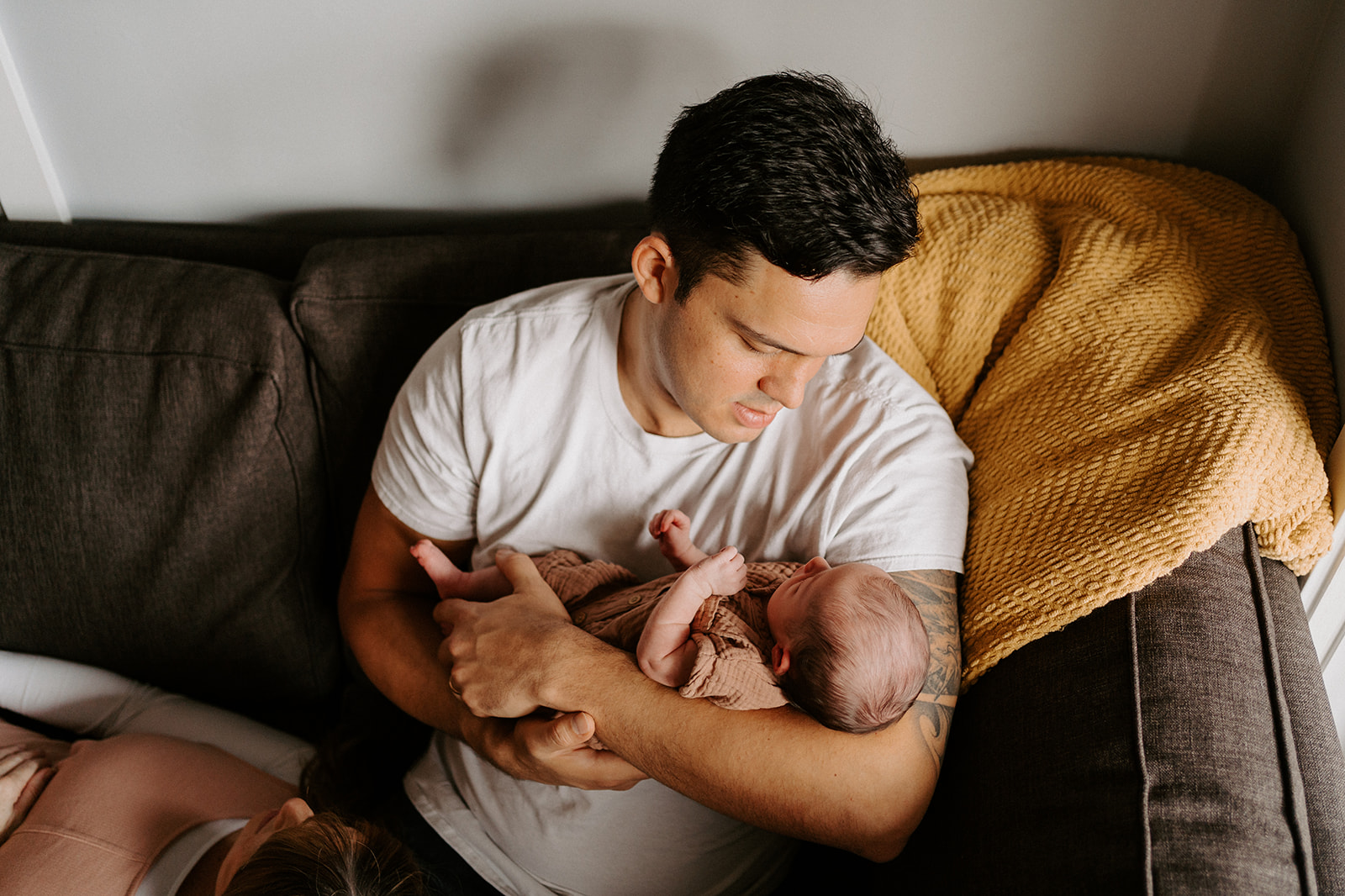 Father holds newborn in his arms while sitting on the couch