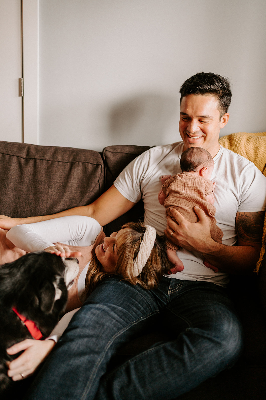 Indoor family newborn session while couple smiles together with newborn and dog