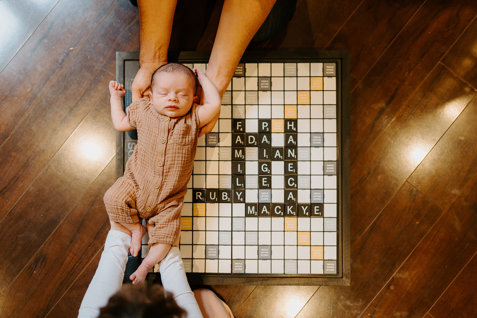 Indoor family newborn session while parents hold newborn over a scrabble board