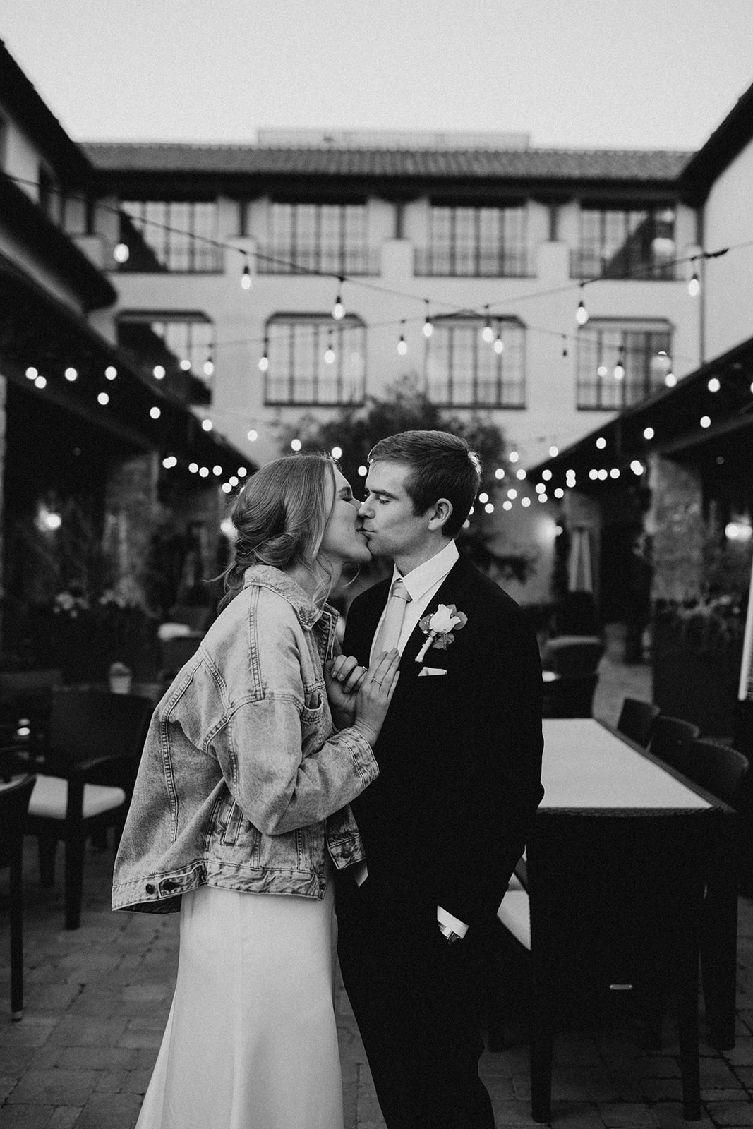black and white photo of just married couple kissing with string lights behind them