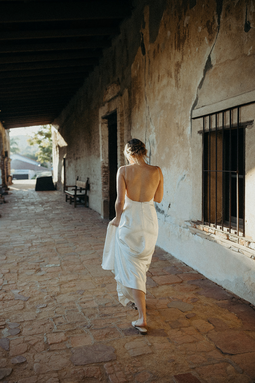bride with backless wedding dress walking through the mission san juan capistrano