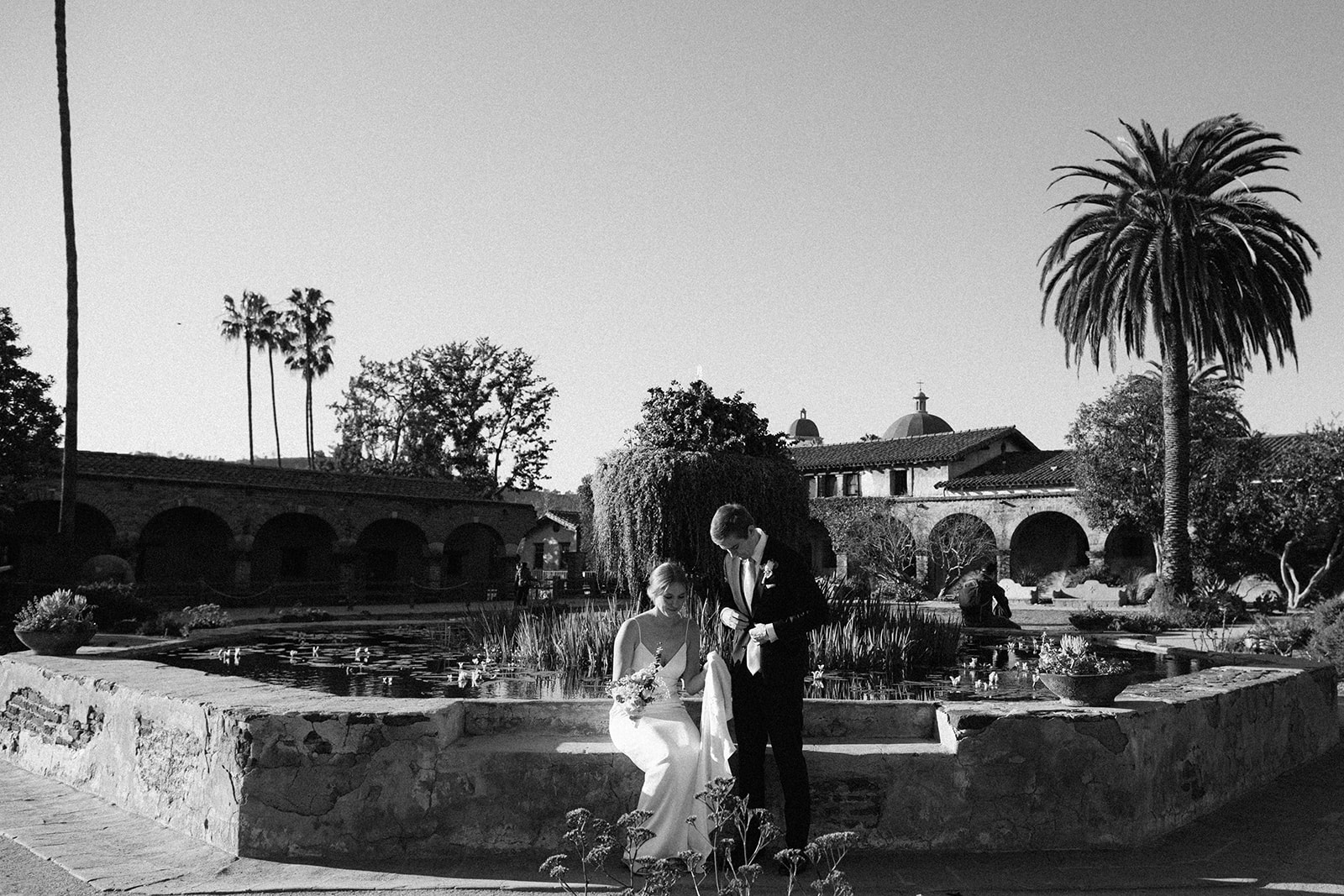 couple sitting near a pond at the mission san juan capistrano