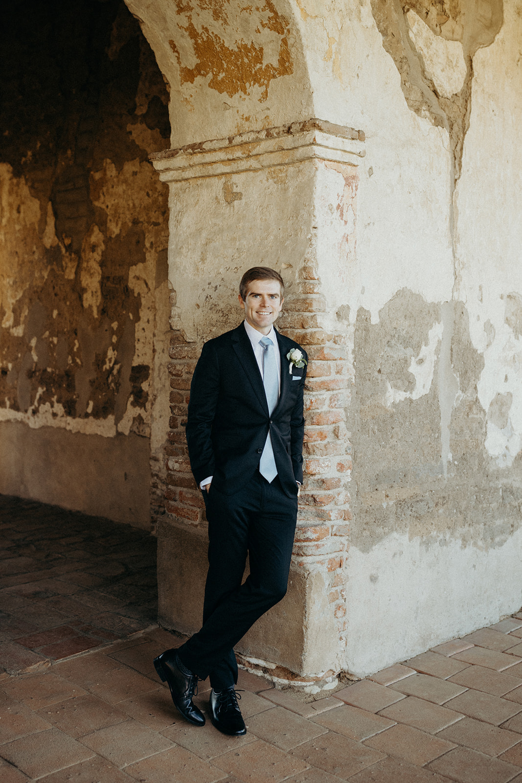 groom leaning against wall at the mission san juan capistrano