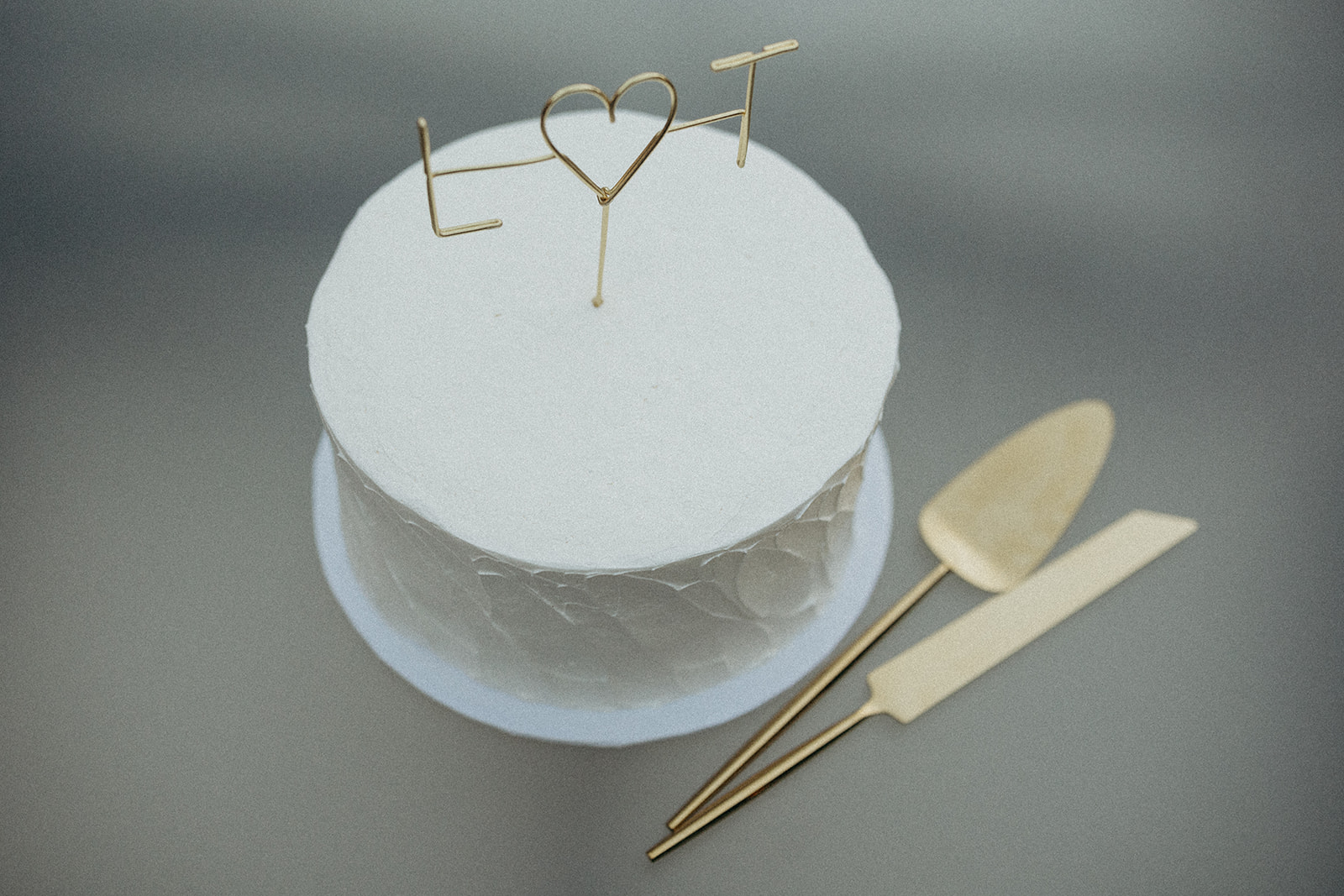 simple white wedding cake with gold topper and gold knife set