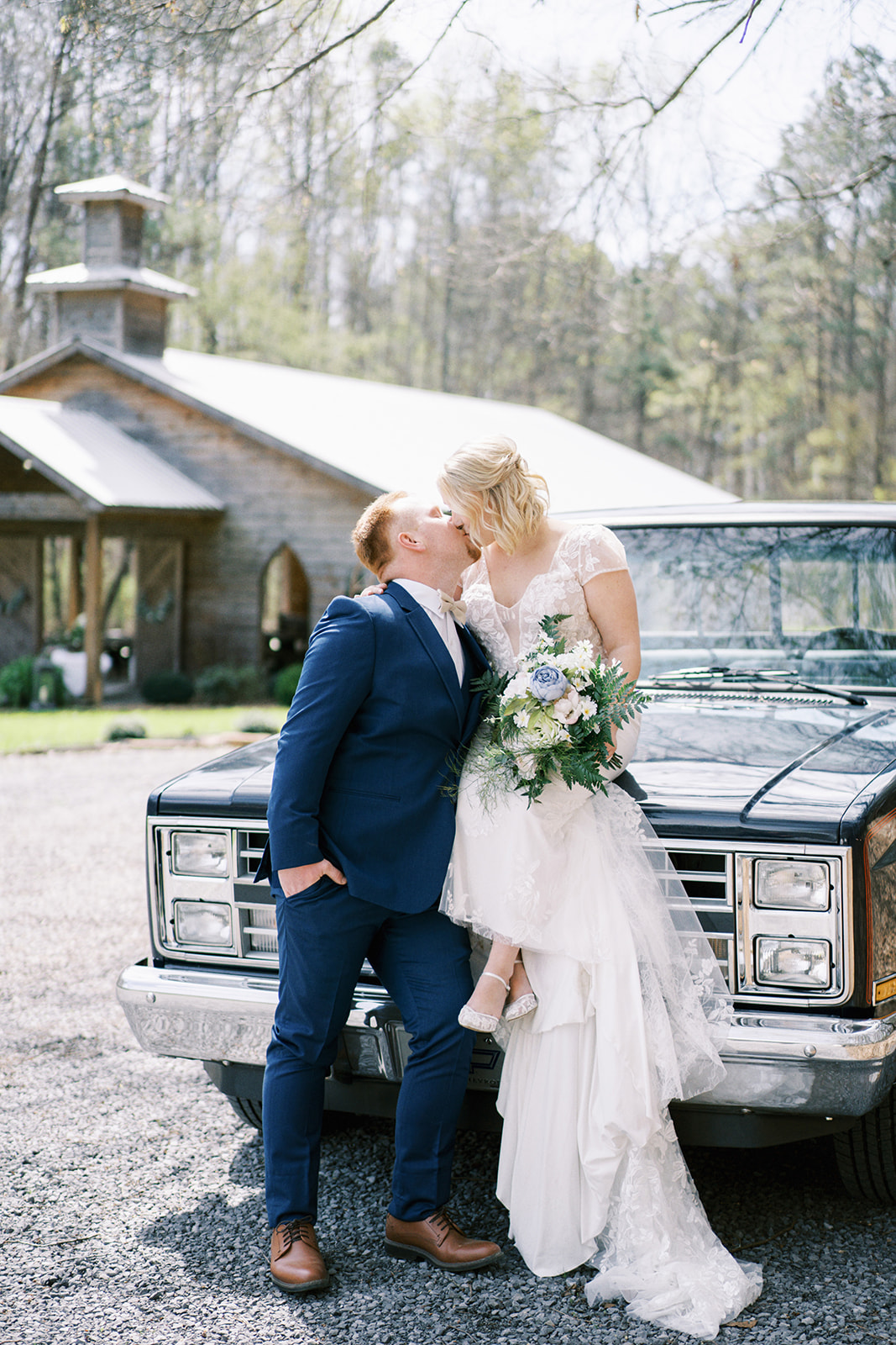 The bride sits on her old Chevrolet truck as she kisses her groom on their wedding day at Dry Creek Chapel