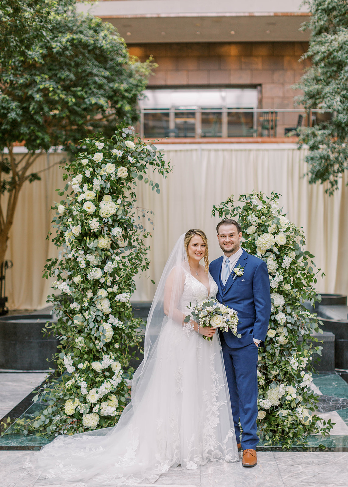 bride and groom pose in front of floral arch