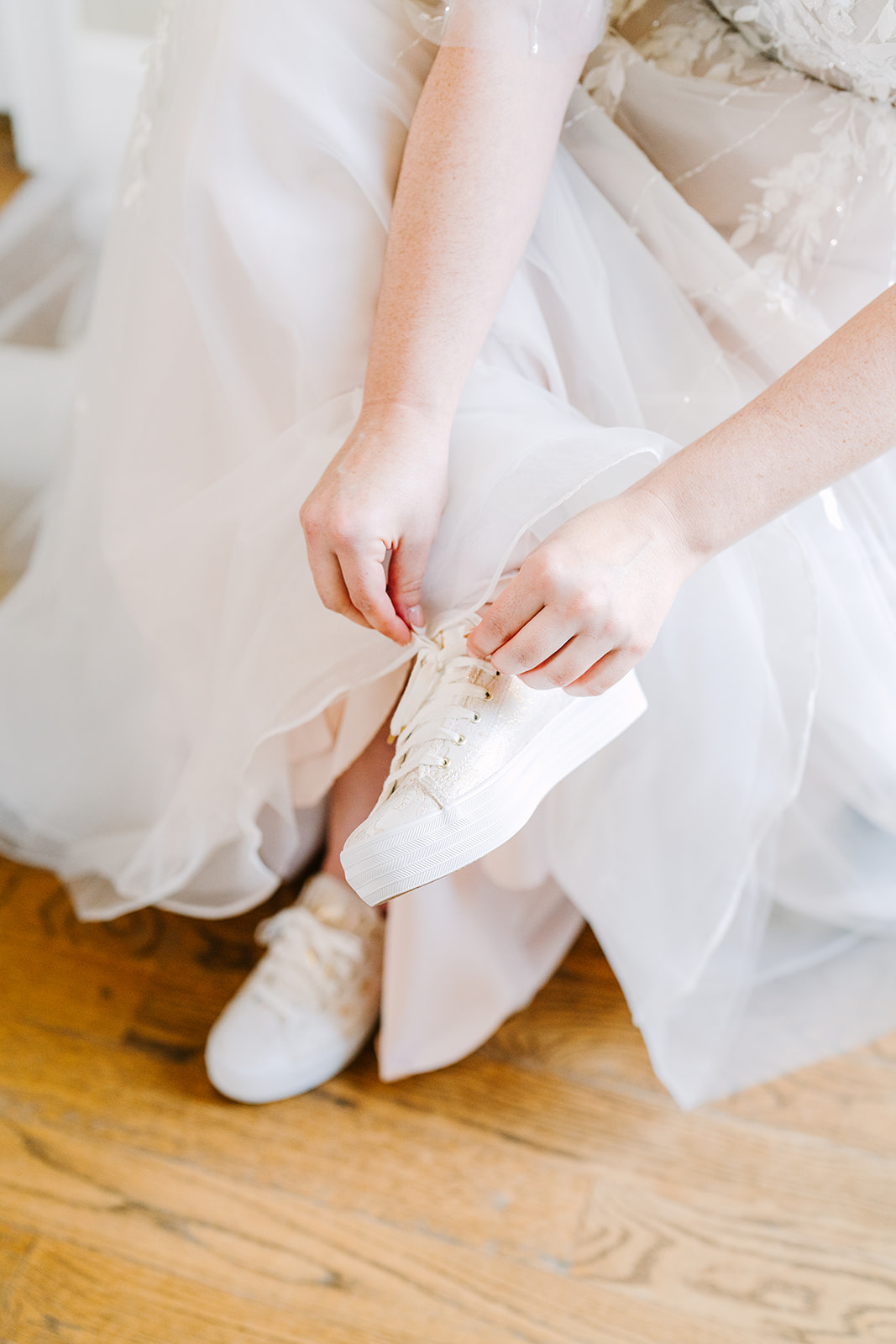 Bride tying her sparkly Keds wedding shoes