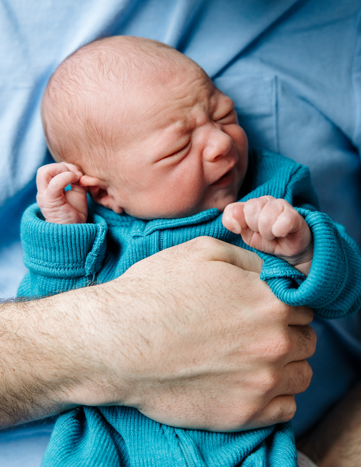 closeup of newborn baby boy with squished up face being held by dad