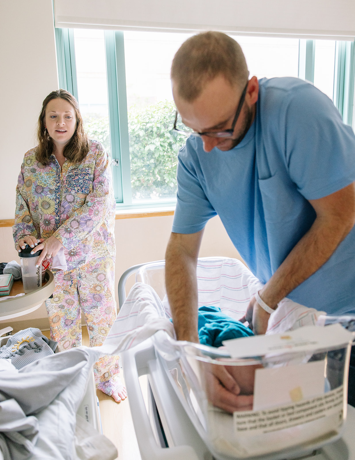 dad swaddling newborn baby boy in hospital while mom looks on