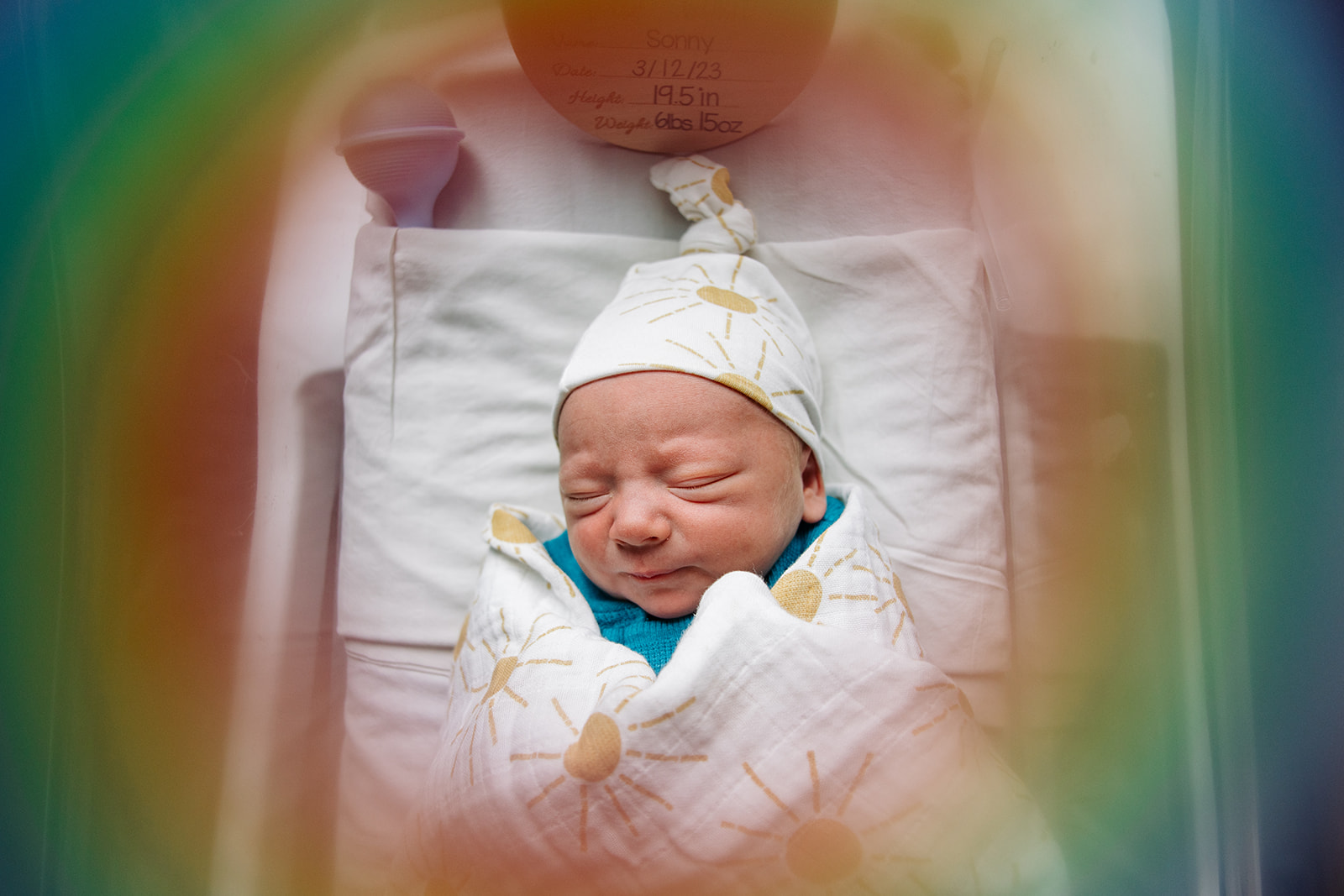 newborn photo of baby in hospital bassinet with rainbow colors all around